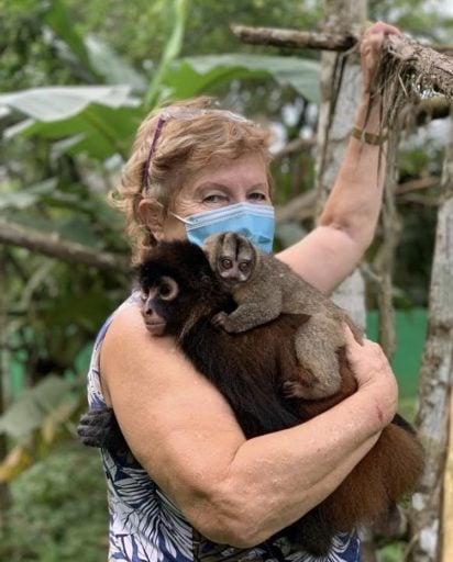 Woman holding a mother monkey with her baby clutching on her back.
